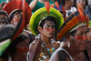 Indigene aus dem Amazonas, Fokus auf eine männlich-präsentierende Person mit einem gelb-grünen Kopfschmuck und roten Akzenten