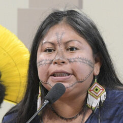 Alessandra Korap Munduruku spricht in ein Mikro. Sie trägt lange Ohrringe und ein dunkelblaues T-Shirt. Ihre langen dunklen Haare sind offen.