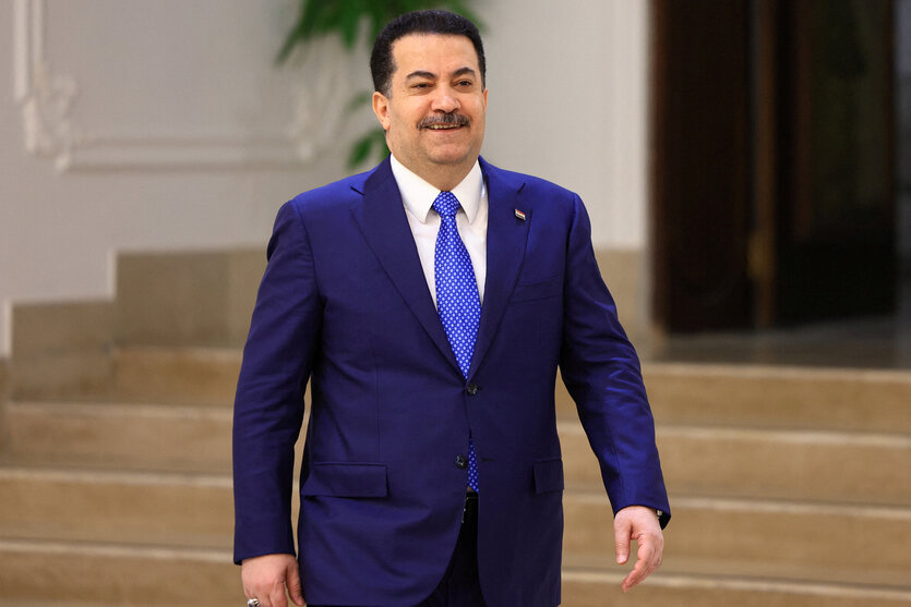 Der irakische Premierminister Mohammed Shia al-Sudani geht lächelnd in einem blauen Anzug in einem Raum