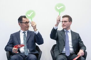 Zwei Männer sitzen nebeneinander und halten grüne Schilder hoch
