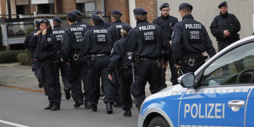 PolizistInnen laufen durch eine Straße, im Vordergrund ein Polizeiauto.