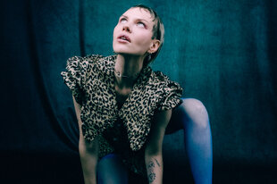 Eine Frau in blauen Strumpfhosen und Leopardenjacke verrenkt sich