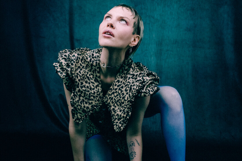 Eine Frau in blauen Strumpfhosen und Leopardenjacke verrenkt sich