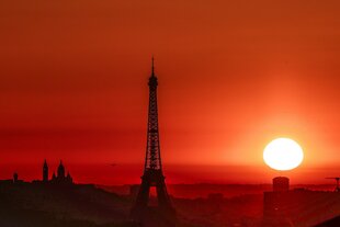 Silhouette des Eiffelturms bei einem leuchtend roten Sonnenuntergang über Paris. Die Sonne steht tief am Horizont und taucht den Himmel in intensive Orangetöne.