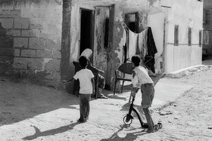 Zwei Kinder, eins mit einem Roller, vor einem sehr einfachen Haus