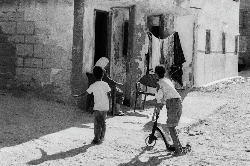 Zwei Kinder, eins mit einem Roller, vor einem sehr einfachen Haus