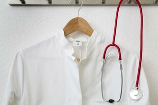 Ein Ärztekittel hängt an einem Haken an der Wand