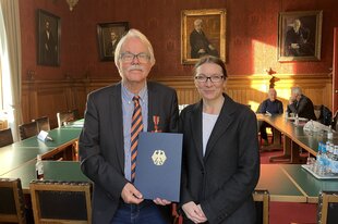 Hans-Peter de Lorent und Schulsenatorin Ksenija Bekeris (SPD) stehen im Hamburger Rathaus und halten eine Urkunde