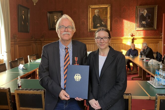 Hans-Peter de Lorent und Schulsenatorin Ksenija Bekeris (SPD) stehen im Hamburger Rathaus und halten eine Urkunde