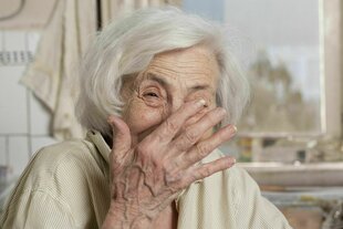 Eine Seniorin lacht und hält sich dabei die Hand vor ihr Gesicht