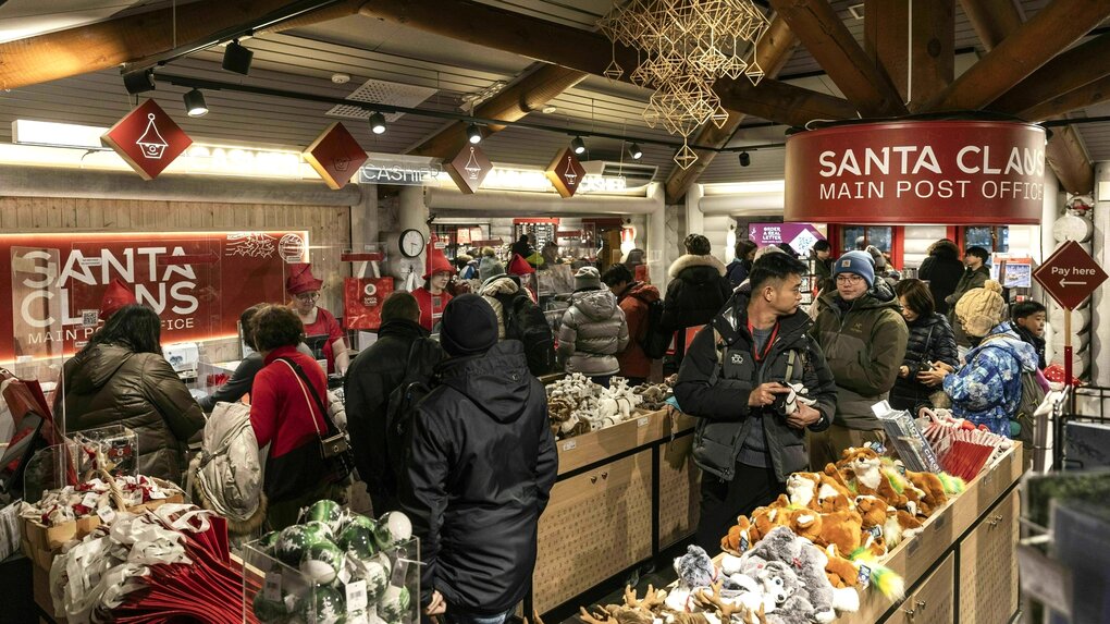 Touristen in warmen Mänteln stehen dicht gedrängt zwischen Holzkisten die mit Weihnachtssachen und Plüschtieren befüllt sind - Von der Decke hängt eine Lampe mit der Aufschrift: Santa Claus - Main Post Office