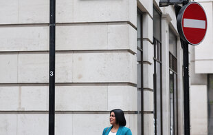 Eine Frau vor einer Hauswand blickt nach rechts. Über ihr ein Einbahnstraßenschild