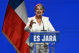 Eine Frau in weißem Anzug steht an einem Rednerpult