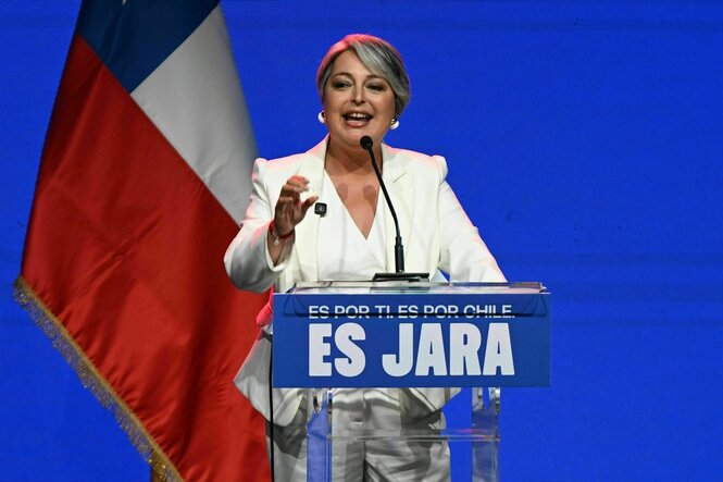 Eine Frau in weißem Anzug steht an einem Rednerpult