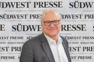 Südwest Presse"-Geschäftsführer Andreas Simmet, hellgraue Haare und Brille mit schwarzem Rahmen, trägt ein graues Sakko und ein weißes Hemd. Im Hintergrund der Bildmontage prangt vielfach der schwarze Schriftzug „Südwest Presse“ auf weißem Grund.