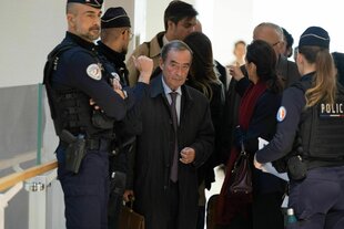 Ein Mann mit Aktentasche steht in einer Gruppe von Polizist:innen