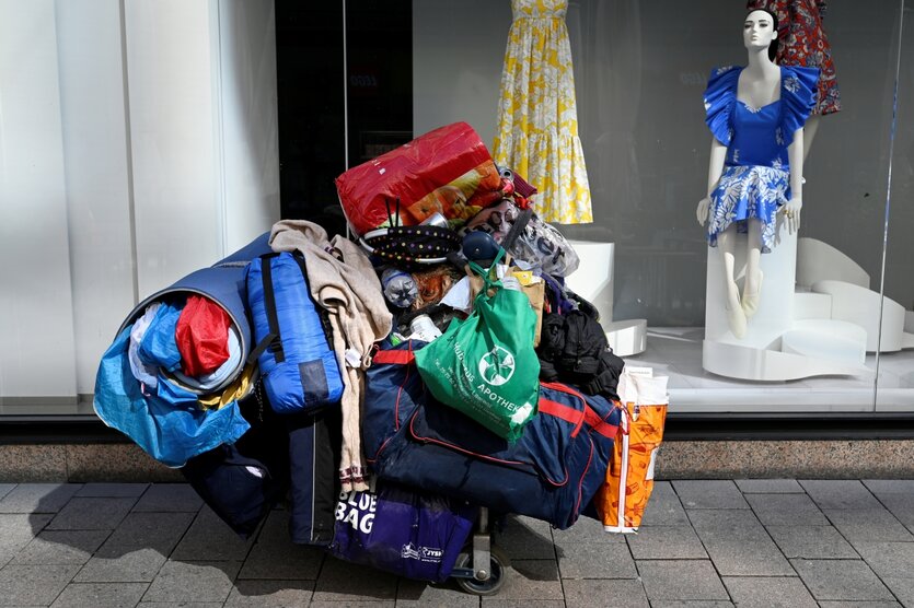Die Habseligkeiten eine obdachlosen Person steht vor einem Schaufenster mit feinen Kleidern