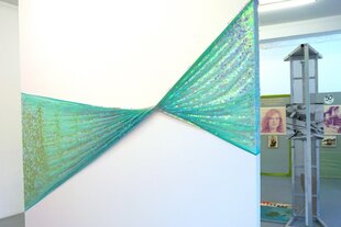 Über eine weiße Wand ist ein Tuch mit Pallietten gespannt. In der Mitte ist es verdreht