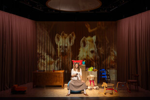 Eine Frau mit Hyämnenohren sitzt zwischen Kinderspielzeug