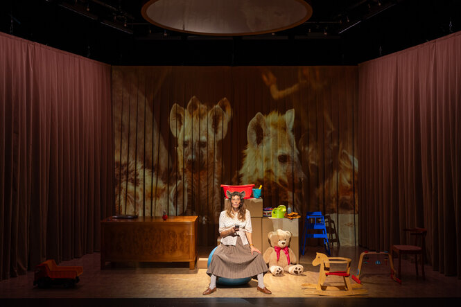 Eine Frau mit Hyämnenohren sitzt zwischen Kinderspielzeug