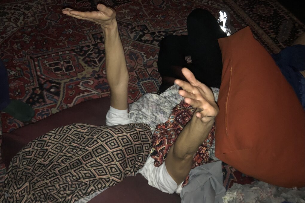 Eine Person liegt zwischen Kleiderhaufen, die Hände nach oben gestreckt