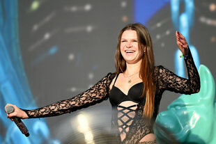 ikkimel steht mit Mikro auf einer Bühne und wird von Scheinwerfern angestrahlt