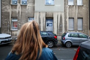 Eine Frau steht vor einem Mehrfamilienhaus.