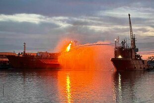 Ein brennender Tanker in einem Hafen.