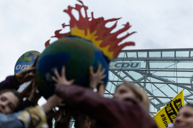 Teilnehmer:innen einer Protestaktion halten eine brennende Erde vor dem Konrad-Adenauer-Haus.