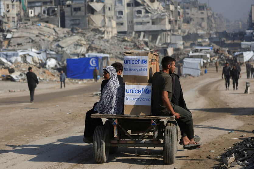 Menschen fahren auf einem beladenen Wagen durch eine Trümmerlandschaft.