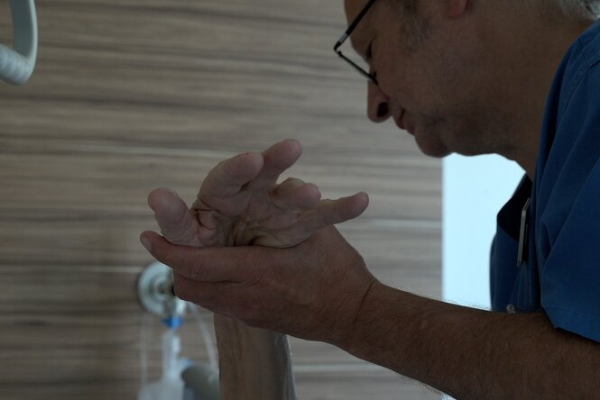 Ein Pfleger hält die Hand einer alten Person im Krankenbett.