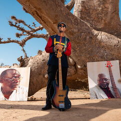 Malick Sy, Bassist von Orchestra Baobab steht mit seinem Bass vor einem Baum