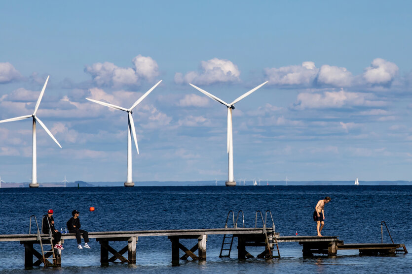Windräder auf dem Meer, davor ein Steg mit Menschen.