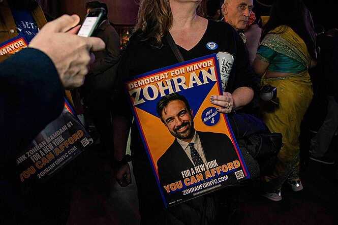 Eine Person hält ein Wahlplakat in den Händen, welches das Porträt eines Mannes zeigt