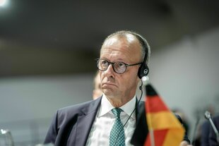 Bundeskanzler Merz mit Kopfhörer schaut ernst