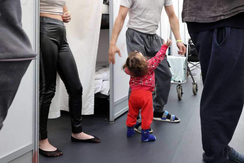 Menschen und ein Kleinkind in rotem Overall in der Flüchtlingsunterkunft im ehemaligen Flughafen Tegel