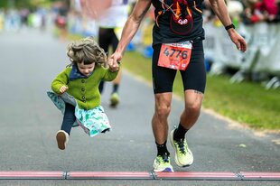 Ein Marathonteilnehmer läuft mit seiner kleinen Tochter an der Hand durchs Ziel
