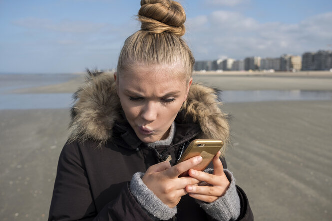 Eine Person schaut auf ihr Smartphone und verzieht das Gesicht
