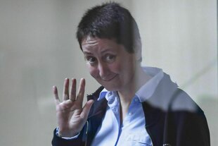 Eine Frau winkt lächelnd in die Kamera