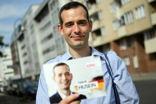 Timur Husein hält einen Flyer von sich in die Kamera
