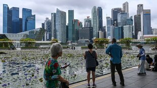 Menschen stehen vor der Skyline von Singapur, eine Frau im Vordergrund hält ein Smartphone in den Händen