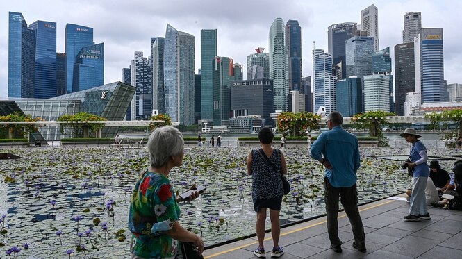Menschen stehen vor der Skyline von Singapur, eine Frau im Vordergrund hält ein Smartphone in den Händen