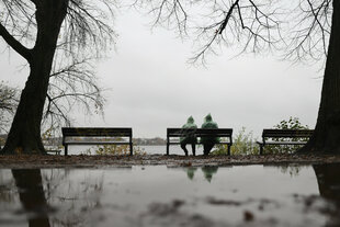 Zwei Menschen mit grünen Regenponchos sitzen bei leichtem Dauerregen auf einer Bank an der Außenalster.