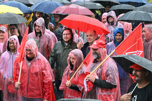 Menschen stehen bei einer Kundgebung im Regen.