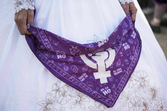 Eine Person im weißen Brautkleid hält ein Tuch in den Händ, auf dem ein feministisches Zeichen abgebildet ist