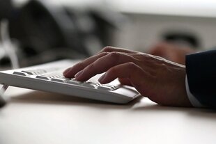 Männerhand auf der Tastatur eines Computers in einem Büro