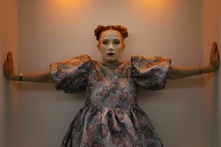 Monetochka im farbenfrohen Kostüm streckt ihre beiden Arme senkrecht an enge Wände. Das Foto wurde in Zürich vor einem Konzert aufgenommen.