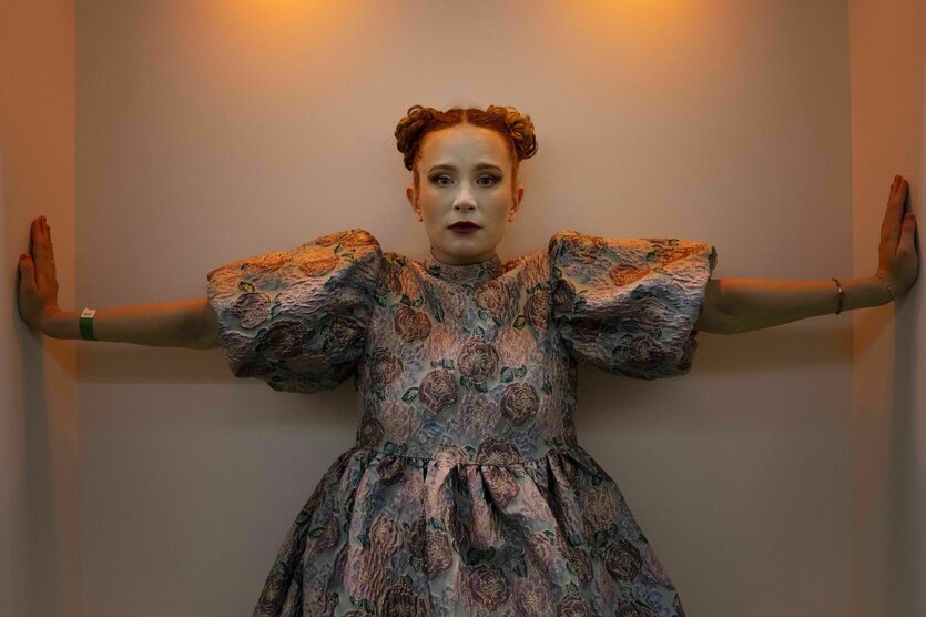 Monetochka im farbenfrohen Kostüm streckt ihre beiden Arme senkrecht an enge Wände. Das Foto wurde in Zürich vor einem Konzert aufgenommen.