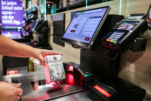 Eine Hand zieht ein Produkt über eine Selbstbedienungskasse im Supermarkt.