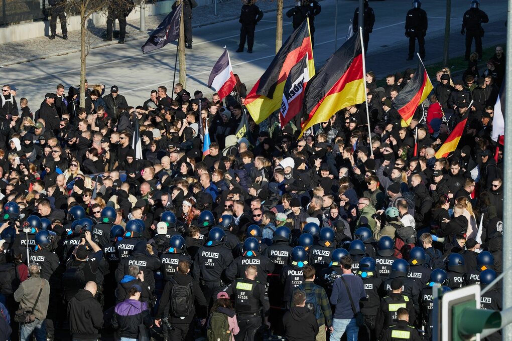 Pulk rechtsextremer Demonstranten mit Deutschland- und Reichsfahnen steht behelmten Polizisten gegenüber